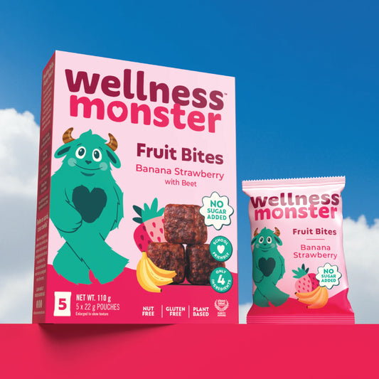 Wellness Monster Banana Strawberry Fruit Bites box and individual pouch on a pink platform against blue sky background